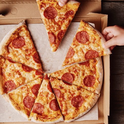 Two hands takes slices of pizza from cardboard box, top view Two hands takes slices of pizza from a cardboard box, top view